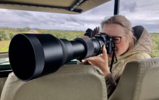 Katharina Rescke fotografiert mit einer großen Teleobjektivkamera aus einem Safari-Fahrzeug.