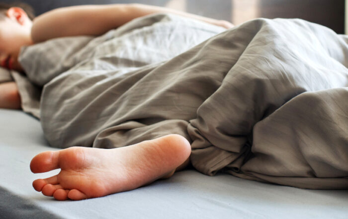Ein Kind schläft friedlich unter einer grauen Decke in einem Bett.