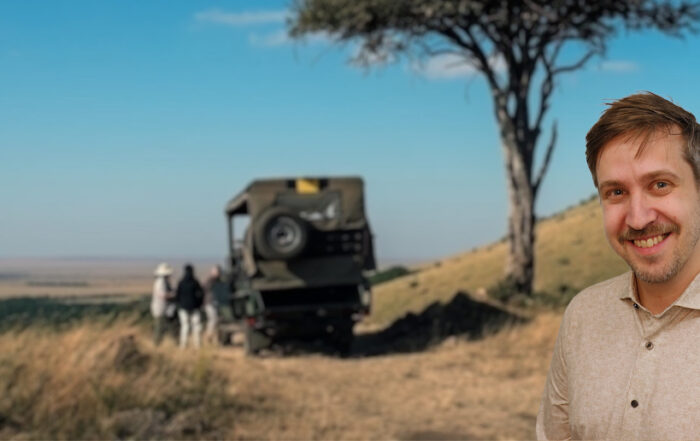 Safari ins Ich: Jonas Schlieter lächelnd vor einer Safari-Landschaft mit Fahrzeug und Baum.